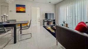 A modern living room with a sofa, a dining table with chairs, a TV, and a chandelier. - Beautiful 2BE/2BA Renovated Apt in Coral Gables (Miami)