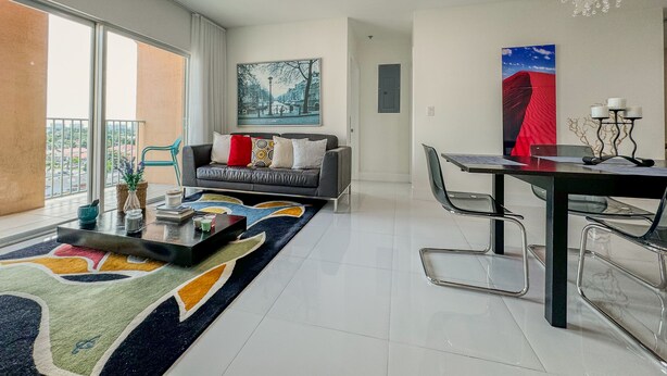 A modern living room with a sofa, a dining table, and chairs. There is a large window providing a view of the outside. - Beautiful 2BE/2BA Renovated Apt in Coral Gables (Miami)