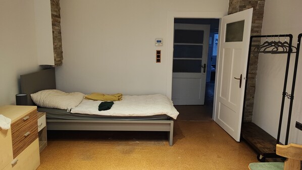 Un dormitorio con cama, mesita de noche, armario y una puerta que da a otra habitación.