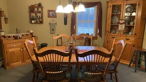 Une salle à manger avec une table et des chaises en bois, un lustre et des meubles en bois dotés de portes en verre.