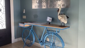 Een blauwe fiets met een houten zadel en rugleuning, een metalen bord met coördinaten, en een decoratief struisvogelfiguur aan een muur.