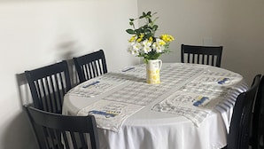 A dining area with a round table covered by a white tablecloth with printed designs, surrounded by black chairs. A vase with yellow flowers is placed on the table.