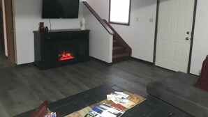 A living room with a fireplace, a television mounted above it, a ceiling fan, and a staircase leading to another level.