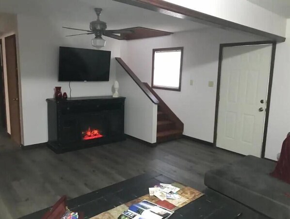 A living room with a fireplace, a television mounted above it, a ceiling fan, and a staircase leading to another level.