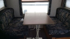Interior compacto de una autocaravana con una mesa central y dos zonas de estar acolchadas.
