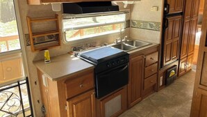 Cocina compacta de autocaravana con armarios de madera, microondas, estufa y lavabo.