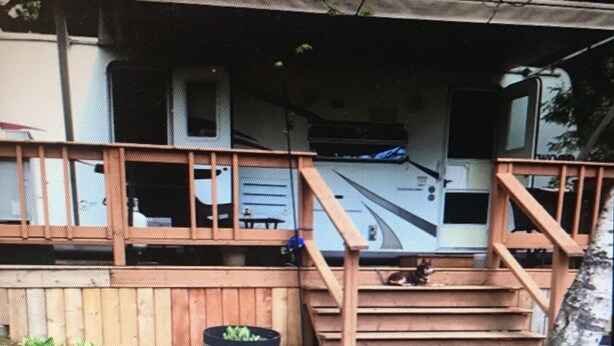 Una escalera de madera que lleva a un porche con una pequeña mesa y un contenedor negro en el suelo.