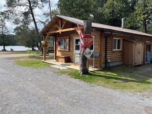A wooden cabin with a porch, a stop sign, and a slow sign. - The Rockwood Trailer/RV - Sandy Beach + Free Watercraft Use in a Natural Setting (Cloyne)