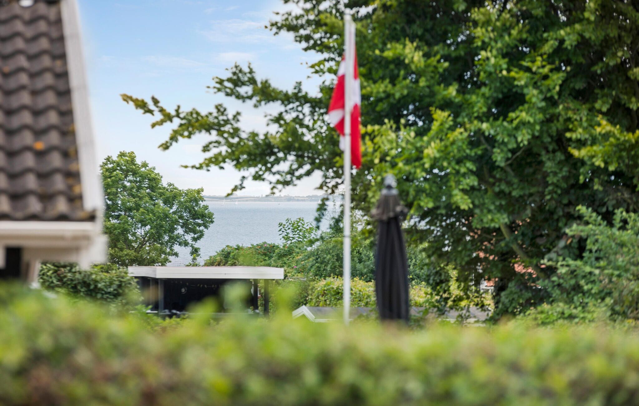 A flagpole with a flag, a body of water, and greenery in the foreground.