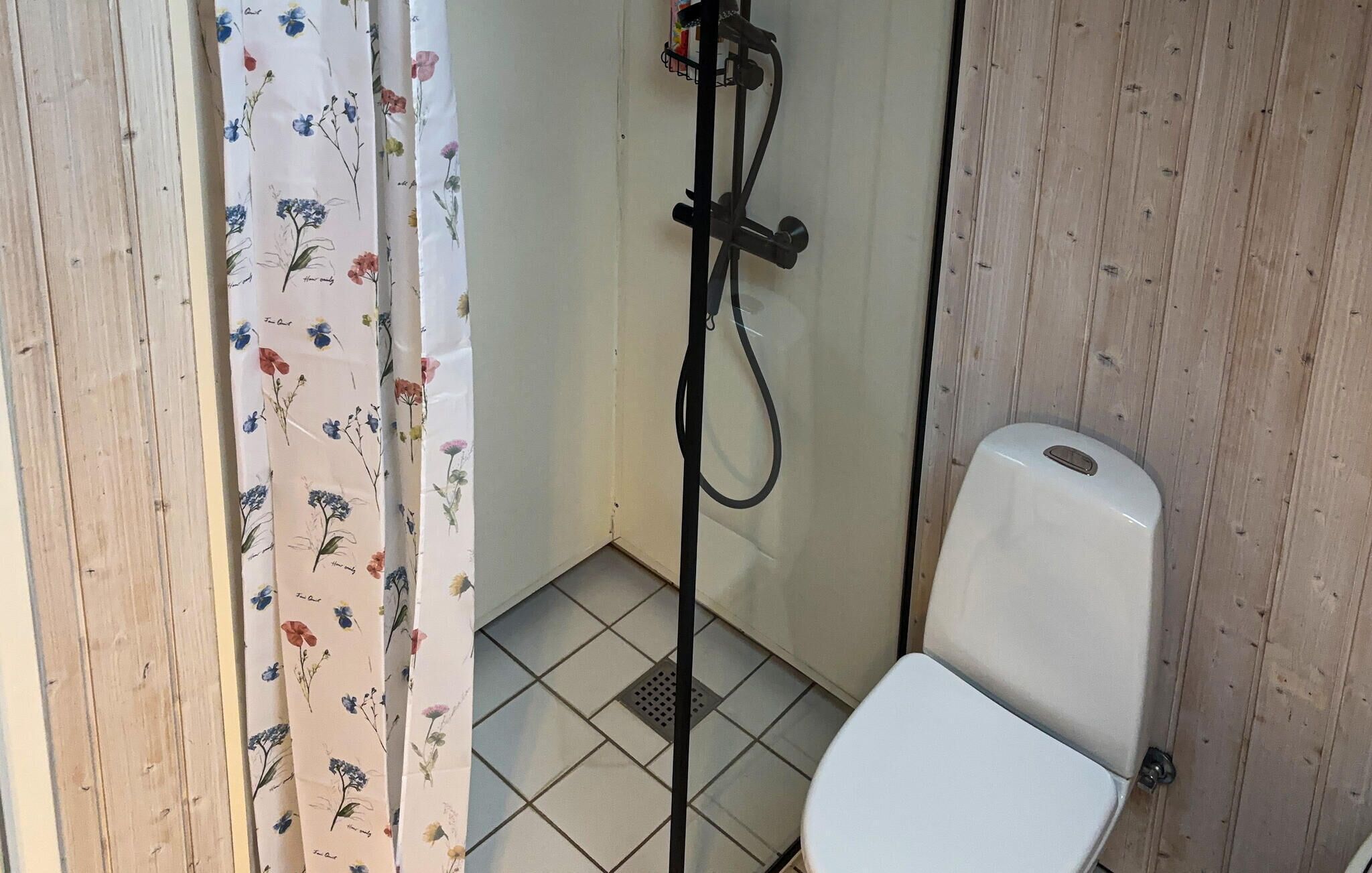 A small, enclosed bathroom with a toilet, a shower, and a curtain with a floral pattern.