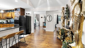A spacious kitchen with wooden cabinets, a black refrigerator, and a bar area with stools. - Spacious open floor plan. 5 beds. 5 TVs. & Art. (Fayetteville)