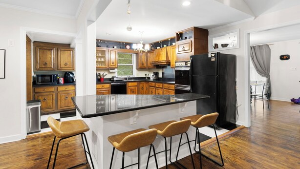 A modern kitchen with wooden cabinets, a central island with bar stools, and a black refrigerator. - Spacious open floor plan. 5 beds. 5 TVs. & Art. (Fayetteville)