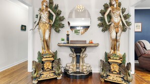 A room with two ornate statues on pedestals, a mirror, and a small table with decorative items. - Spacious open floor plan. 5 beds. 5 TVs. & Art. (Fayetteville)