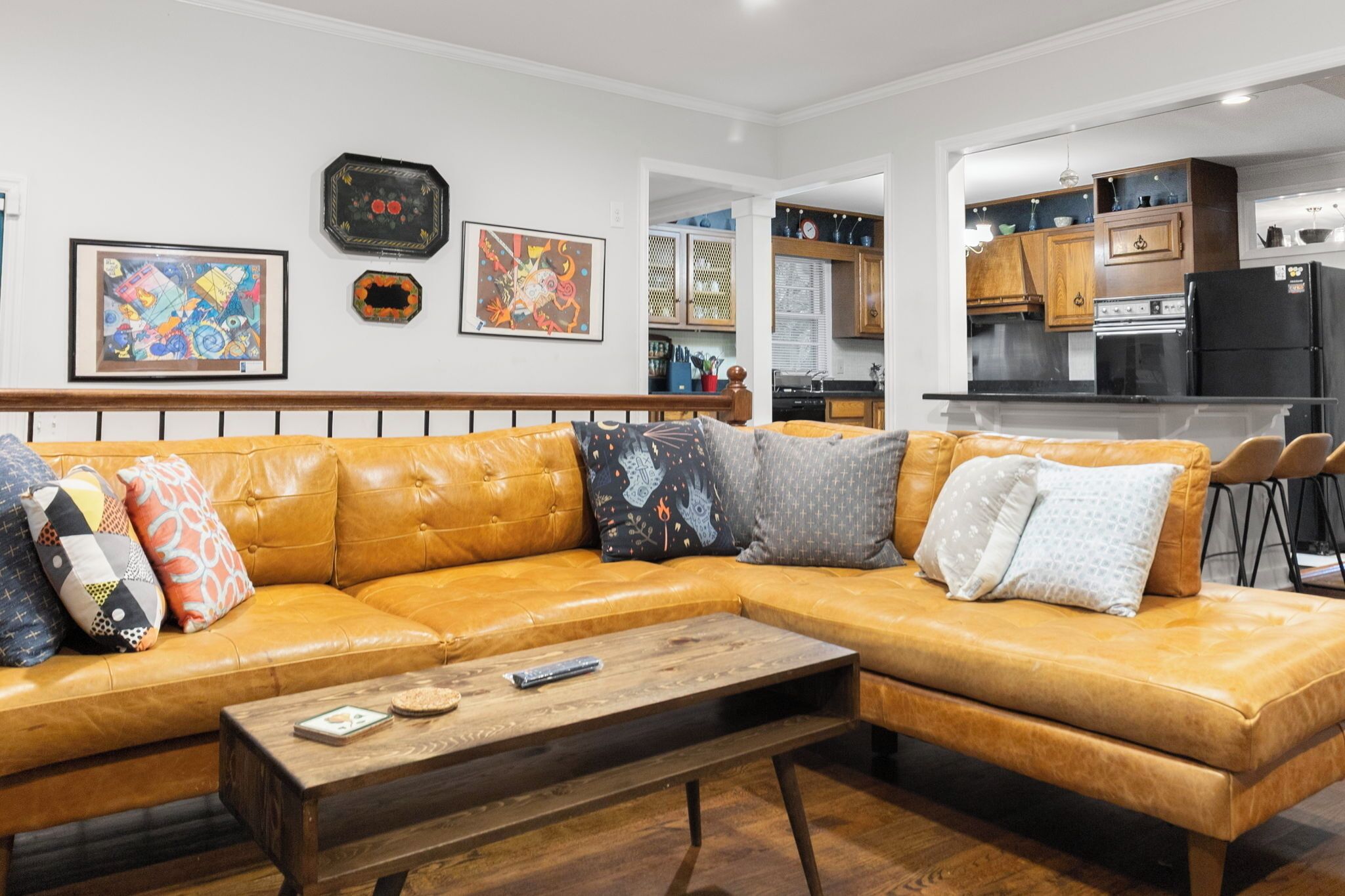 Una sala de estar moderna con un sofá de cuero tipo seccional, una mesa de centro de madera y una cocina al fondo.