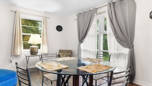 A round glass table with chairs, a blue sofa, and a lamp on a windowsill. - Spacious open floor plan. 5 beds. 5 TVs. & Art. (Fayetteville)