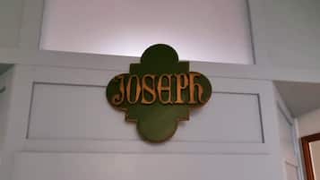 Een houten naambordje met de naam 'Joseph' bevestigd aan een witte muur.