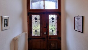 A hallway with a wooden double door with glass panels, a radiator on the left, patterned floor tiles, and a framed certificate on the wall. - Ferienwohnung Josef - Wohnen wie zur Gründerzeit (Kevelaer)