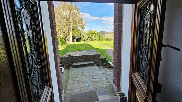 An open doorway leading to a stone pathway, a grassy area, and a brick wall. - Ferienwohnung Josef - Wohnen wie zur Gründerzeit (Kevelaer)