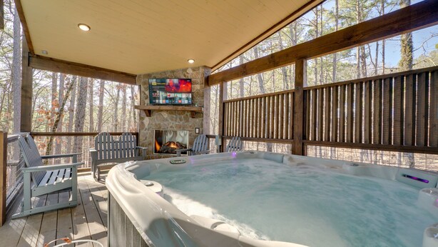 A hot tub area with a stone fireplace, wooden deck, and outdoor seating. - Two King Suites, Bunk Loft with Games, Hot Tub (Broken Bow)
