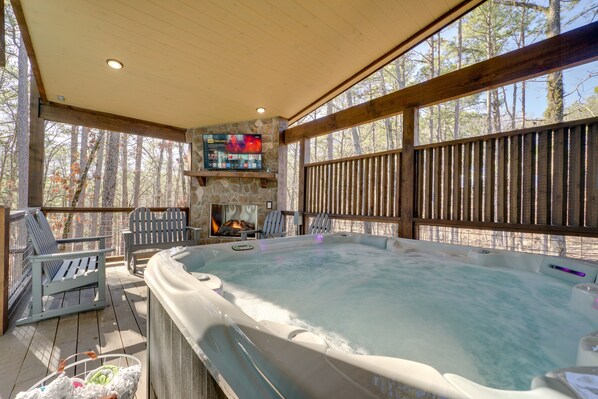 A hot tub area with a stone fireplace, wooden deck, and outdoor seating. - Two King Suites, Bunk Loft with Games, Hot Tub (Broken Bow)