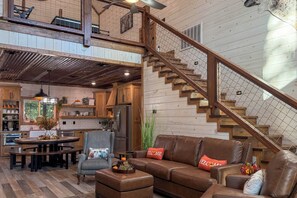 A spacious living area with a wooden staircase, a dining table, and a kitchen in the background. - Two King Suites, Bunk Loft with Games, Hot Tub (Broken Bow)