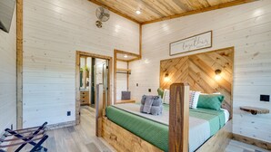 A wooden cabin bedroom with a bed, a wooden headboard, a wall-mounted fan, and a sign above the bed. - Two King Suites, Bunk Loft with Games, Hot Tub (Broken Bow)