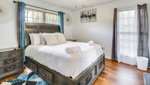 Un dormitorio con una cama grande, un ventilador de techo, una ventana con cortinas y una obra de arte en la pared.