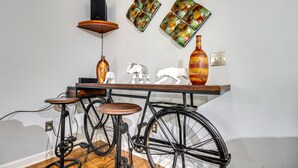 Una habitación con piso de madera, una bicicleta negra, un taburete de madera, una mesa con adornos y una pared con dos obras de arte enmarcadas.
