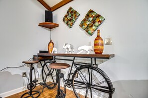 A room with a wooden floor, a black bicycle, a wooden stool, a table with decorative items, and a wall with two framed artworks. - Home 2.5 Mi to Fort Stewart w/ Heated Pool (Hinesville)