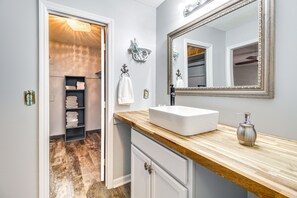 A bathroom with a wooden vanity, white sink, and a large mirror. There is a towel rack with folded towels and a shelf with more towels. - Home 2.5 Mi to Fort Stewart w/ Heated Pool (Hinesville)