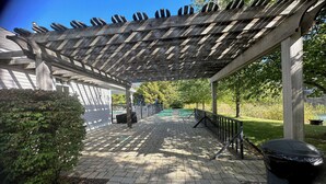 Un espace extérieur abrité, doté d’un chemin en briques, d’une pergola en bois et d’une poubelle.