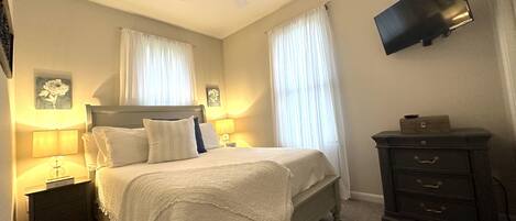 Un dormitorio con cama, mesitas de noche, cómoda, ventilador de techo y televisor de pantalla plana.
