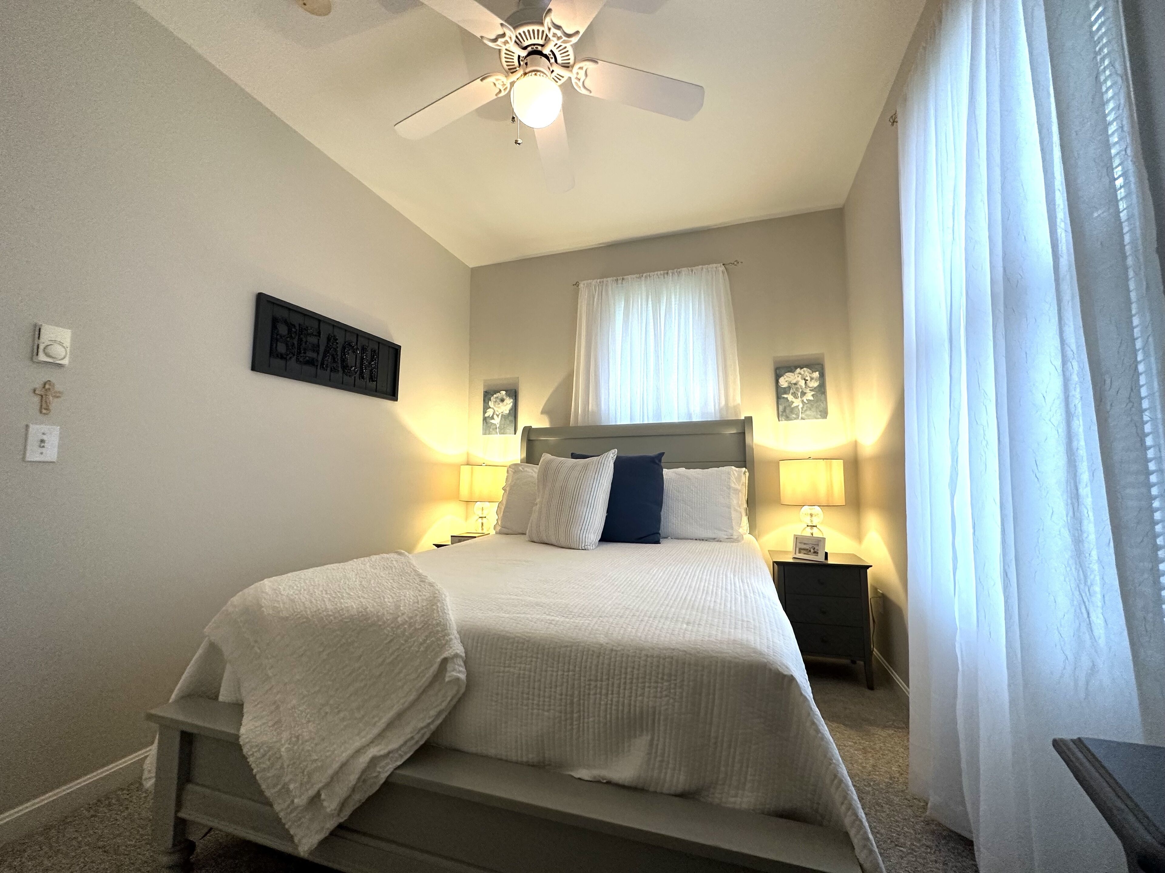Une chambre à coucher avec un lit, un ventilateur de plafond, des lampes de chevet et un panneau accroché au mur.