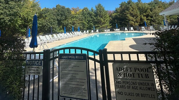 Une piscine pour adultes avec un jacuzzi, entourée de chaises longues et de parasols, et dont les règles sont affichées sur un panneau.