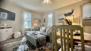 Un salon chaleureux avec un canapé gris, une chaise en bois, un tapis à motifs et un ventilateur de plafond.