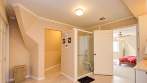 Un'ampia stanza con soffitto alto, cabina doccia in vetro, letto con copriletto rosso e ventilatore a soffitto.