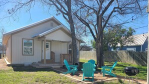 A small house with a porch, two turquoise Adirondack chairs, a grill, and a wooden fence in the background. - Pet-Friendly Home for 7 with Fire Pit (Junction)