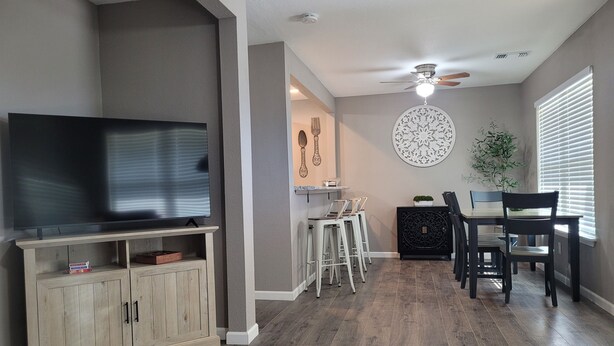 A modern living room with a flat-screen TV, wooden cabinets, a dining area with a table and chairs, and a ceiling fan. - Pet-Friendly Home for 7 with Fire Pit (Junction)