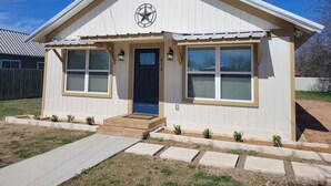 A single-story house with a dark blue front door, two large windows on the ground floor, and a small porch with steps. - Pet-Friendly Home for 7 with Fire Pit (Junction)