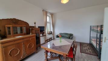 A room with a wooden dining table, a green sofa, a bunk bed, and a wooden dresser.