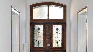 Un couloir doté d’un sol à motifs, d’une porte double en bois avec des panneaux de verre et d’un plafond orné d’une moulure décorative.