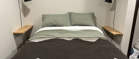 A bed with a geometric-patterned blanket, two pillows, and two bedside tables with lamps.