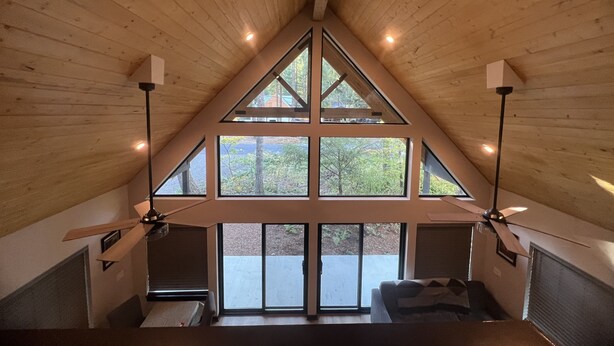 Une chambre à coucher aménagée dans un espace de type « loft », avec un plafond en pente, de grandes fenêtres et un ventilateur de plafond.