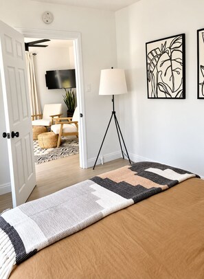 Ein Schlafzimmer mit einem großen Bett, einer Stehlampe, einem Fernseher und einer Tür zu einem anderen Raum.