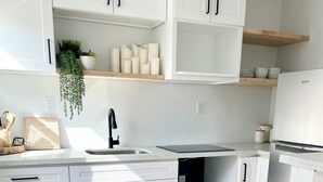 Une cuisine moderne avec des meubles blancs, un robinet noir et un réfrigérateur blanc.