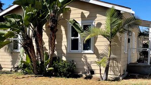 Une maison de plain-pied à la façade beige, avec de grands bananiers et un palmier dans le jardin.