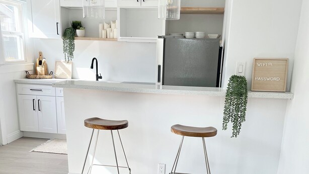 Une cuisine moderne avec des meubles blancs, un réfrigérateur en acier inoxydable et deux tabourets de bar.