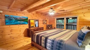 Quarto de cabana de madeira com cama, cômoda, pintura e janela com vista para árvores.