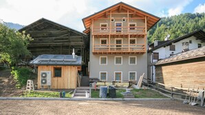 A multi-story building with a wooden facade, a balcony, and a small attached structure with solar panels.
