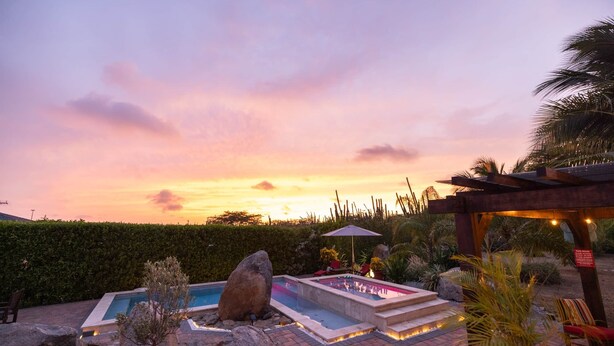 A swimming pool with a pergola and seating area, surrounded by rocks and plants. - Oasis of Relaxation 1BR Apartment w/pool -Sunrise (Noord)